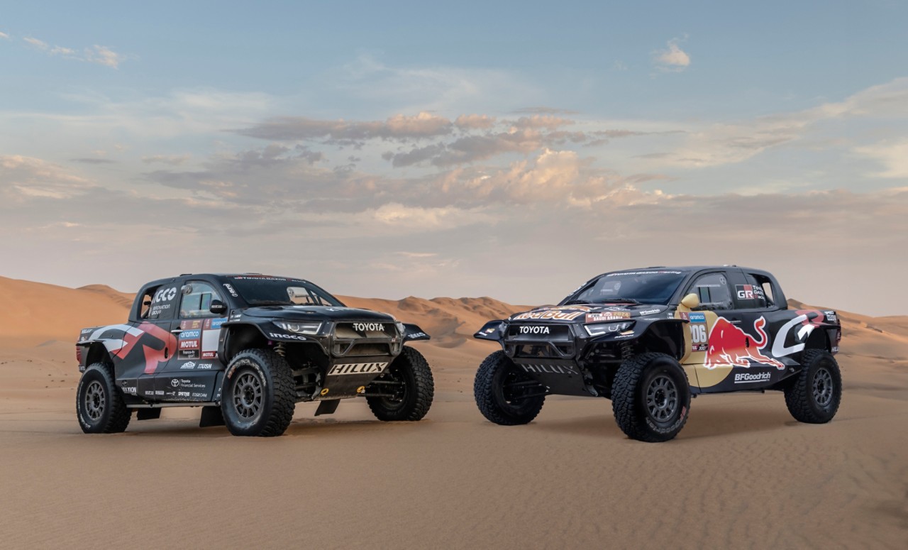Static front 3/4 shots of two Hilux racing models in the desert